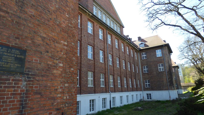 Gdańsk. The Polish Gymnasium. Contemporary photographs. The building of the former Polish Gymnasium. The photograph presents the right wing of the school building constructed from bricks. There are windows on each floor, the attic and the basement. In the background some trees can be observed.