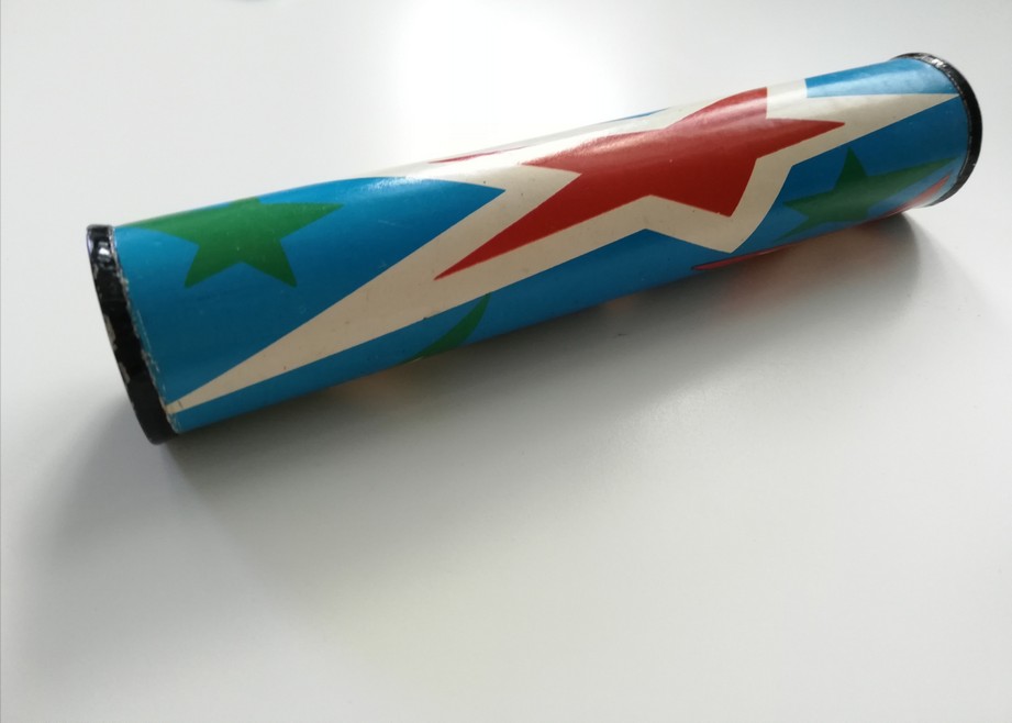 The photograph features an old, slightly battered toy kaleidoscope. It is blue and there are big white and red stars printed on it along with small green stars.